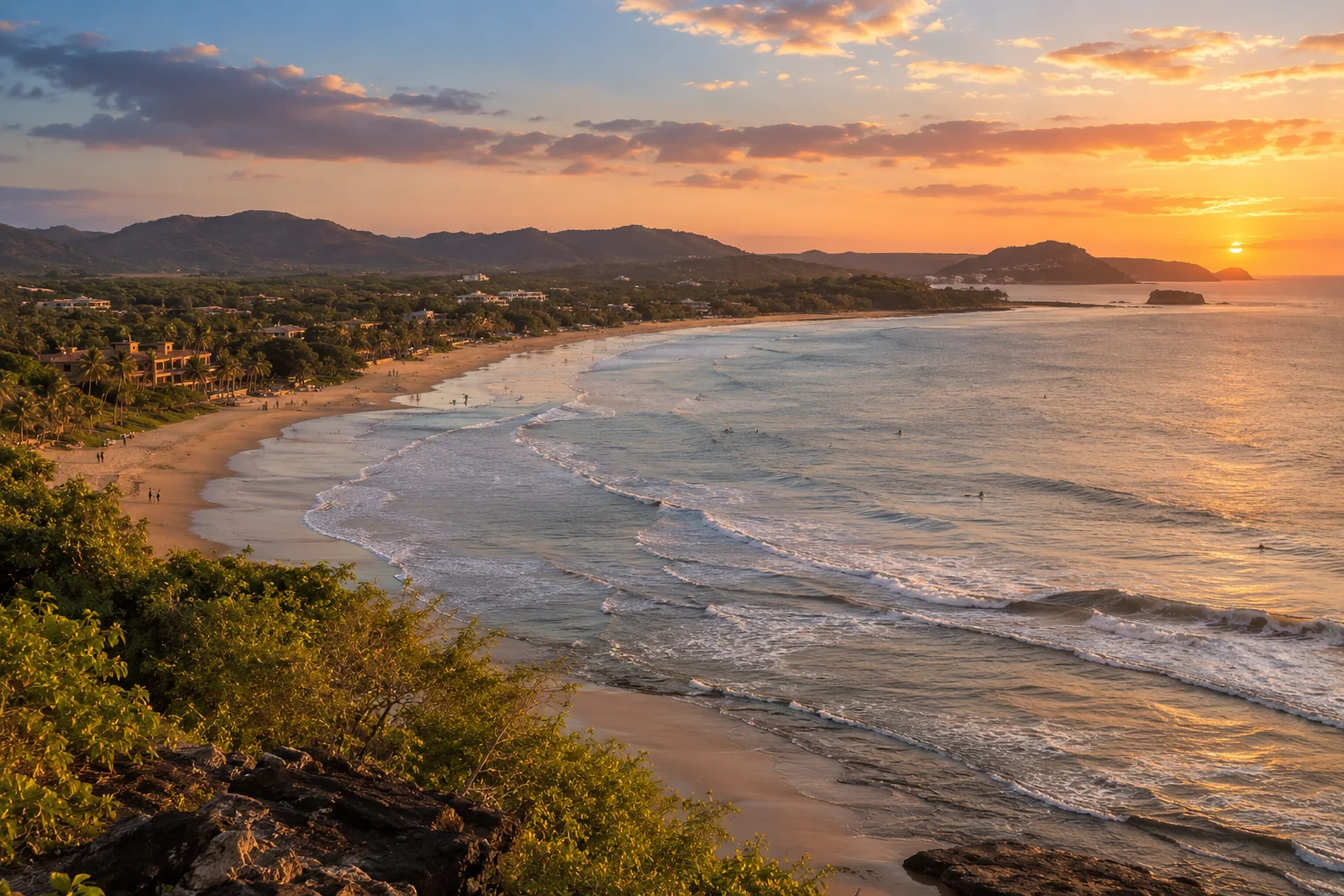 An expansive curved beach with gentle Pacific surf, palms and low-rise coastal town buildings set back from the sand
